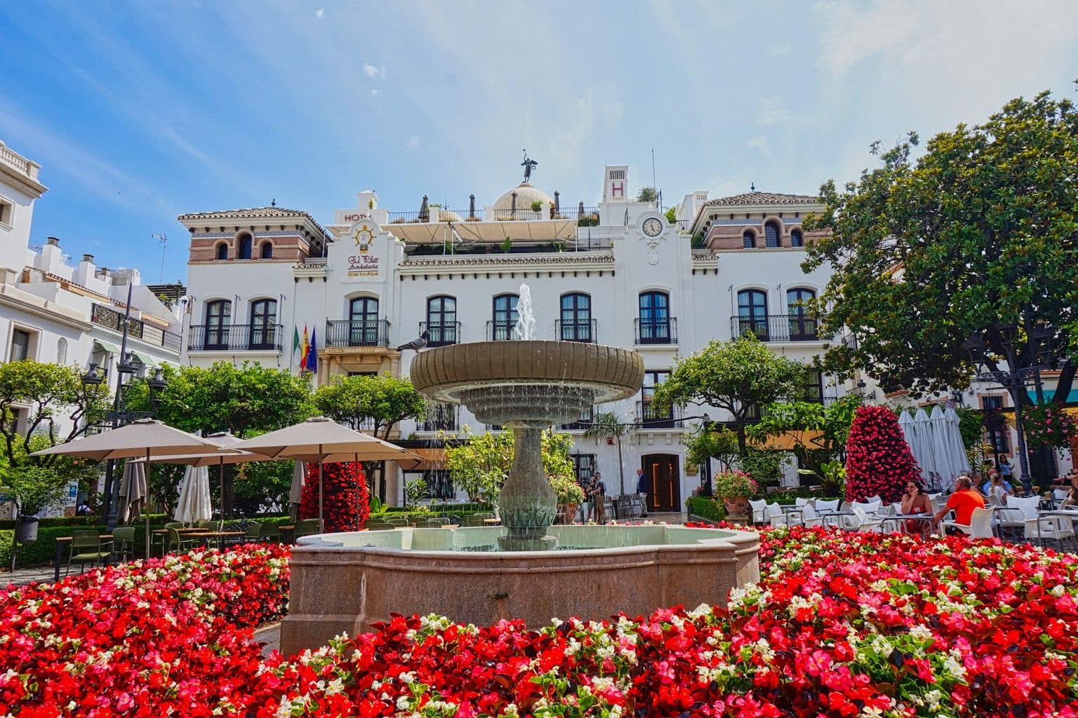Estepona: a square with a fountain and flowers in front of a white façade